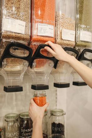 Hands filling jar with lentils from dispensers in zero waste store, promoting eco-friendly shopping.