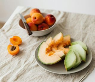 Still life of delicious healthy assorted melons on plate and bowl with fresh ripe apricots placed on linen tablecloth
