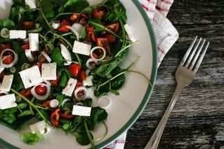 A vibrant and colorful spinach salad with feta cheese and tomatoes on a rustic table.
